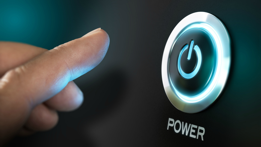 A close-up of a finger pressing a glowing blue power button on a black surface. The button is encircled with a metallic ring, and the word POWER is displayed below it in white text.