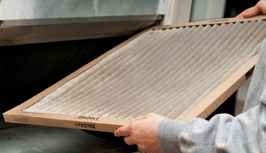 A person holding a dusty air filter, removing it from an HVAC system. The filter has visible dirt on its pleated surface, emphasizing the need for regular cleaning or replacement to maintain air quality.